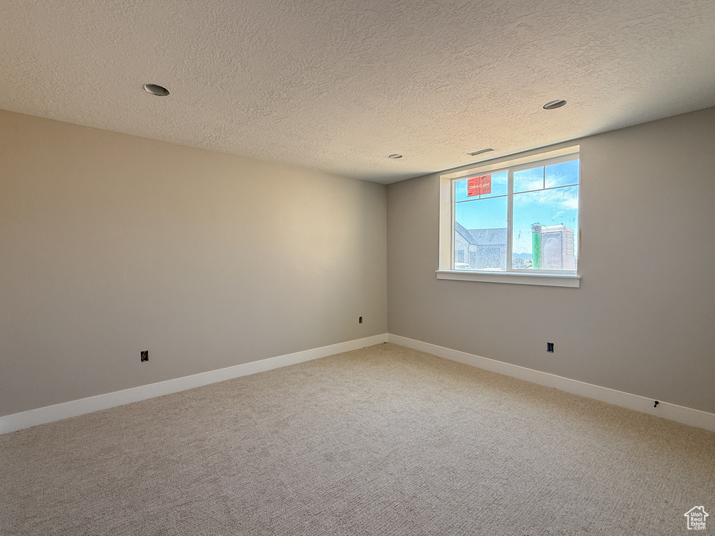 Unfurnished room with light carpet, baseboards, and a textured ceiling