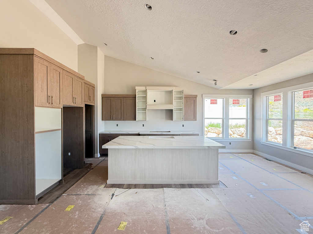 Kitchen featuring a textured ceiling, a kitchen island, vaulted ceiling, open shelves, and light stone counters