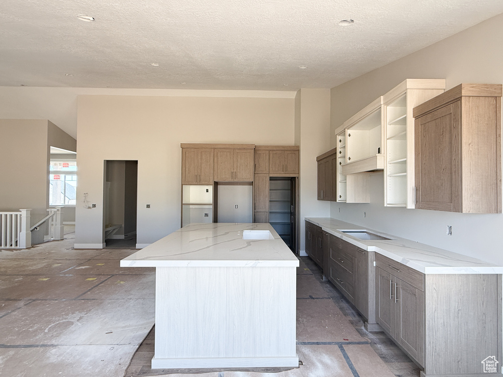 Kitchen featuring a center island, stovetop, a textured ceiling, open shelves, and light stone countertops