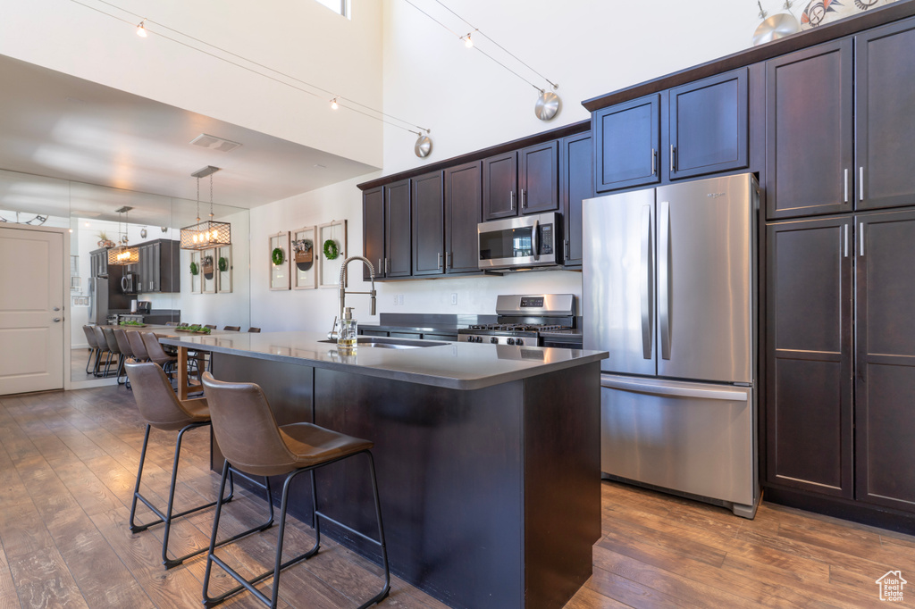 Kitchen featuring appliances with stainless steel finishes, a sink, dark countertops, a breakfast bar, and dark wood finished floors