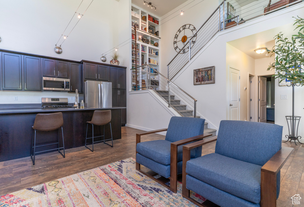 Living room with a high ceiling, stairs, dark wood-style flooring, and baseboards
