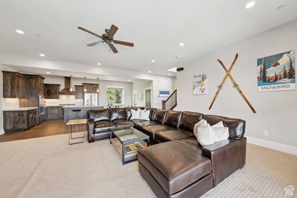 Living room with recessed lighting, a ceiling fan, baseboards, light carpet, and stairway