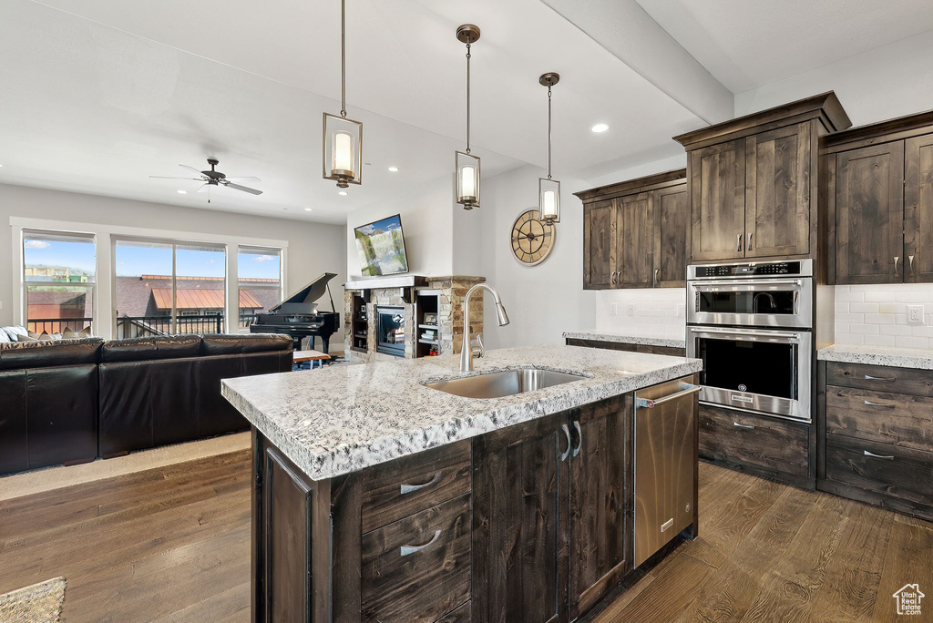 Kitchen featuring a sink, appliances with stainless steel finishes, dark wood finished floors, dark brown cabinets, and open floor plan