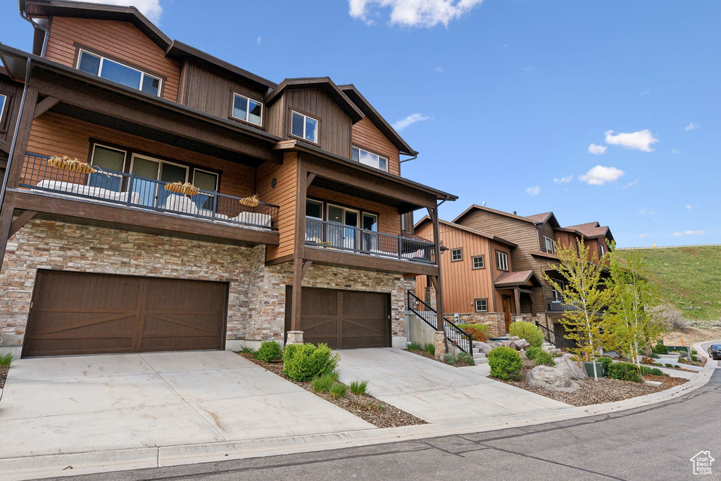 View of front of house featuring stone siding, a balcony, an attached garage, and concrete driveway