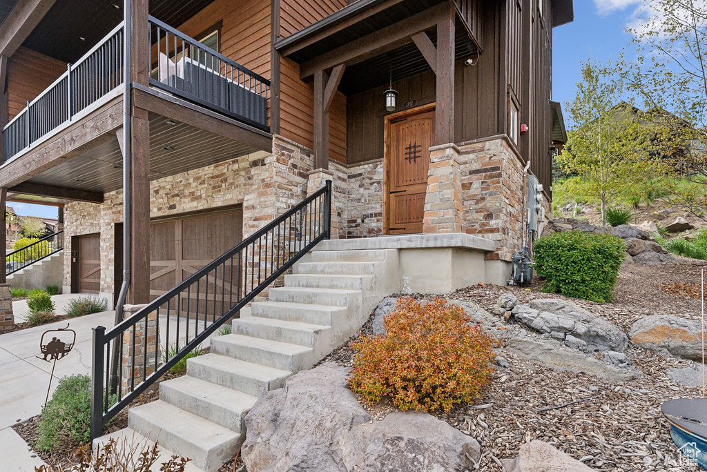 Entrance to property with stone siding, board and batten siding, and a balcony