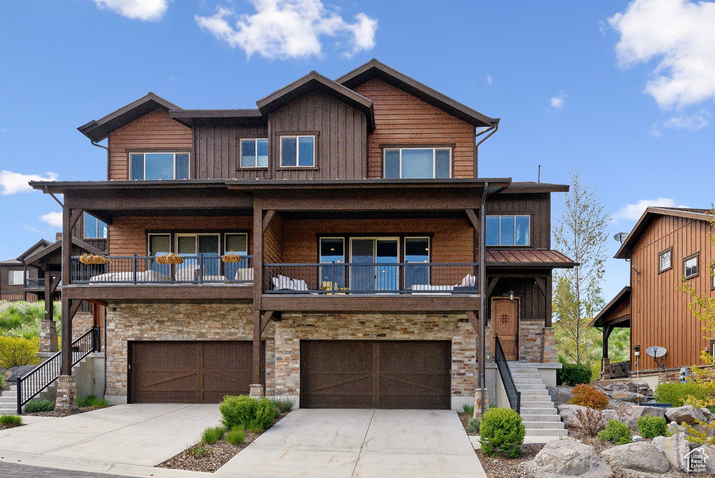 Chalet / cabin featuring stairs, an attached garage, stone siding, driveway, and a balcony