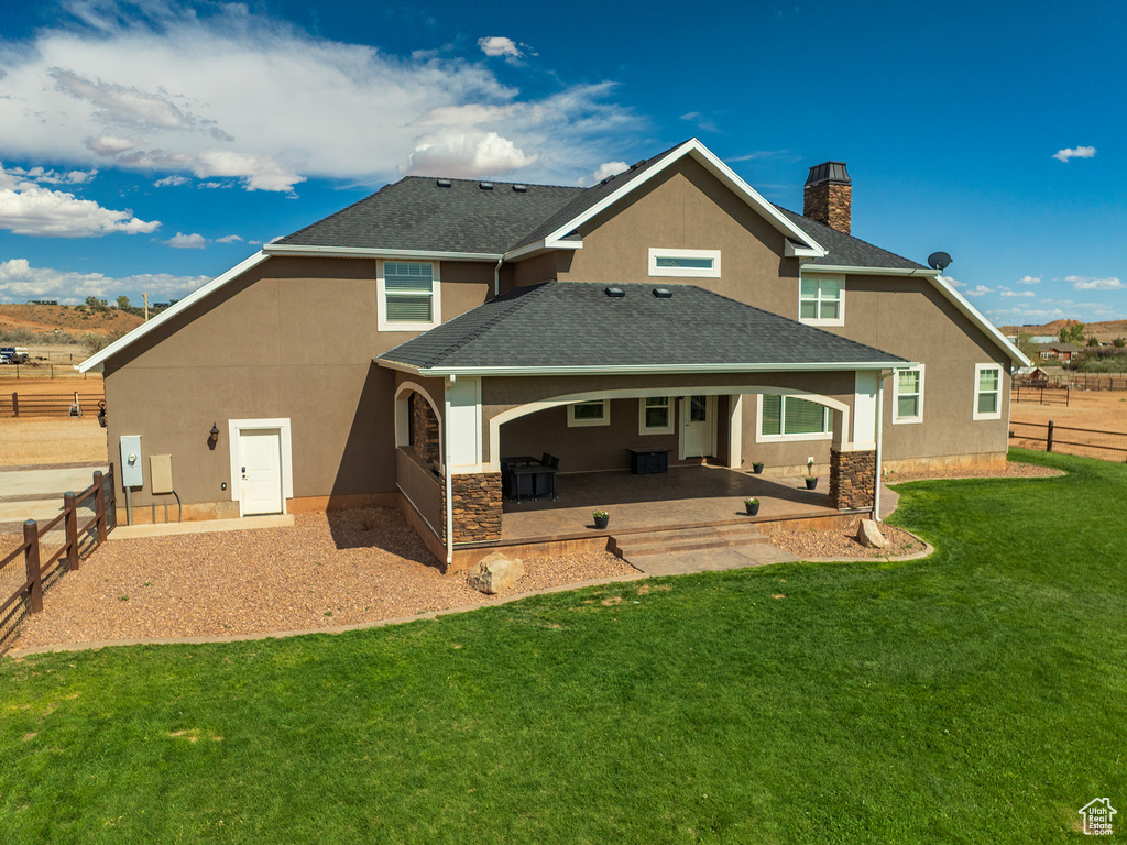 Back of house with stucco siding, a patio, roof with shingles, a chimney, and stone siding