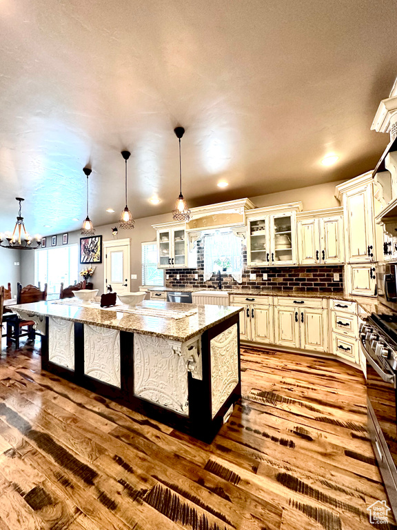 Kitchen featuring hardwood / wood-style floors, a chandelier, decorative backsplash, stainless steel range with gas stovetop, and decorative light fixtures