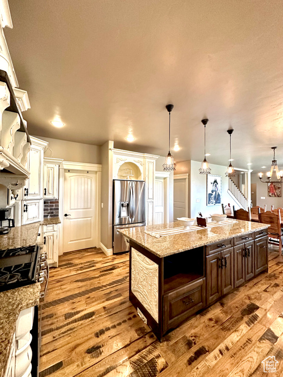 Kitchen with appliances with stainless steel finishes, light wood-style floors, a kitchen island, dark brown cabinets, and a chandelier