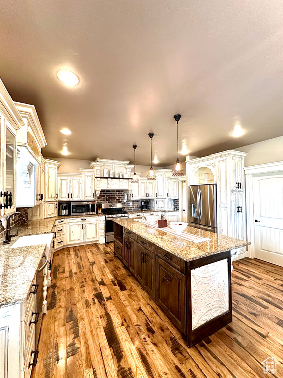 Kitchen featuring appliances with stainless steel finishes, a sink, wood-type flooring, dark brown cabinetry, and a large island