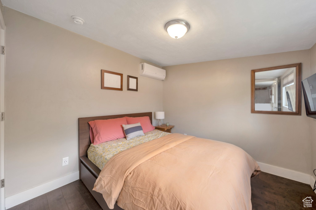 Bedroom with a wall mounted AC, baseboards, and dark wood-style floors