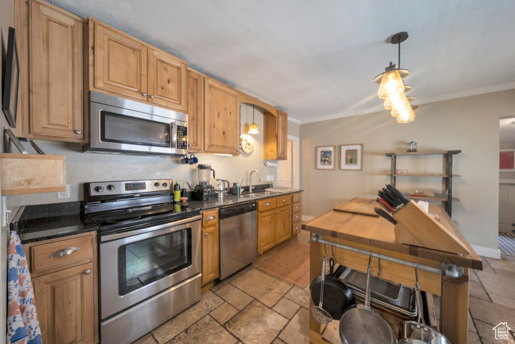 Kitchen with appliances with stainless steel finishes, crown molding, stone tile floors, pendant lighting, and a sink