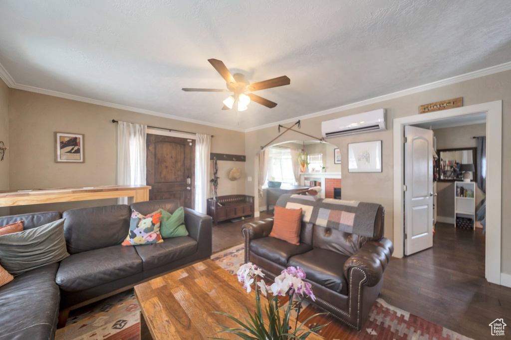 Living room with an AC wall unit, wood finished floors, a ceiling fan, crown molding, and arched walkways