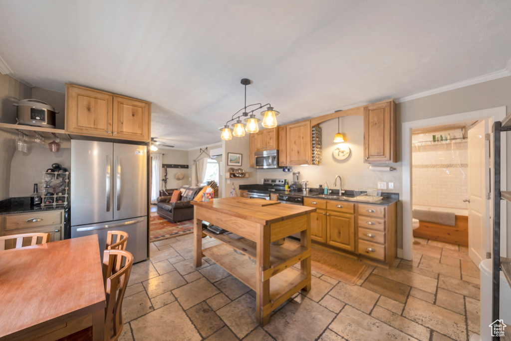 Kitchen with stainless steel appliances, stone tile flooring, crown molding, a ceiling fan, and a sink