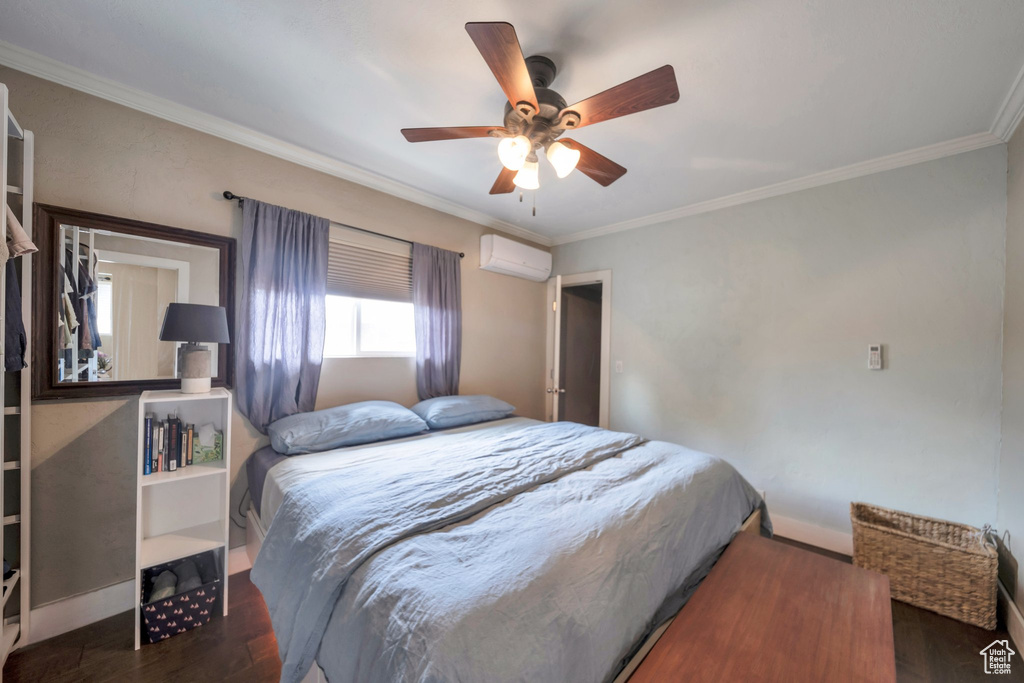 Bedroom with a wall mounted AC, wood finished floors, ornamental molding, baseboards, and a ceiling fan