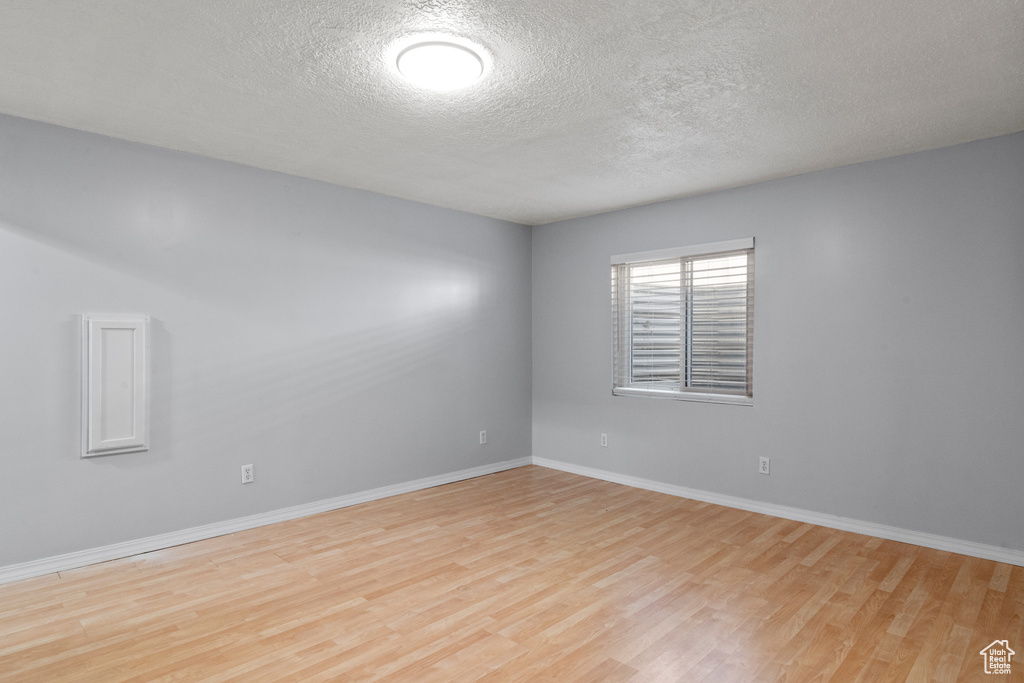 Spare room featuring wood finished floors, a textured ceiling, and baseboards