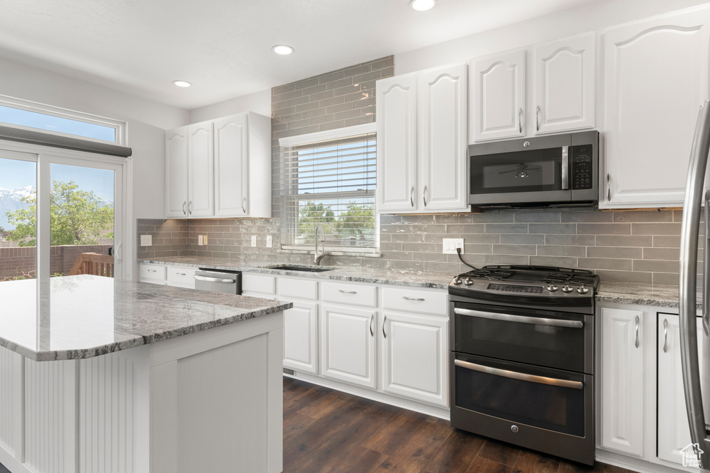 Kitchen with appliances with stainless steel finishes, a sink, decorative backsplash, recessed lighting, and light stone counters