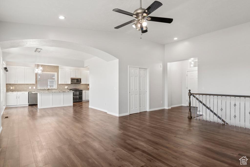 Unfurnished living room featuring dark wood-style floors, a ceiling fan, arched walkways, recessed lighting, and a sink