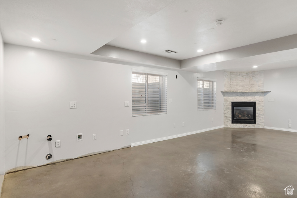 Unfurnished living room featuring concrete flooring, a fireplace, baseboards, recessed lighting, and a raised ceiling