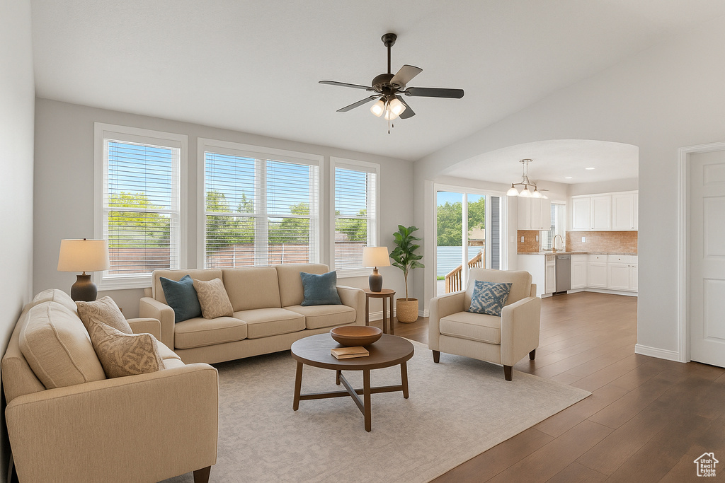 Living area featuring dark wood-style floors, lofted ceiling, a ceiling fan, arched walkways, and a chandelier