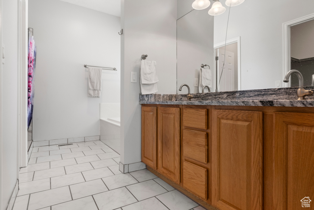 Full bath featuring double vanity, a garden tub, a spacious closet, and tile patterned flooring