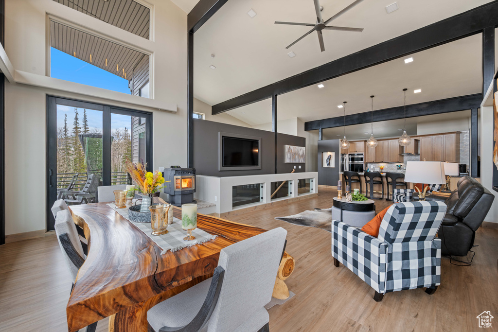 Living room featuring beam ceiling, light wood-style flooring, a ceiling fan, a wood stove, and high vaulted ceiling