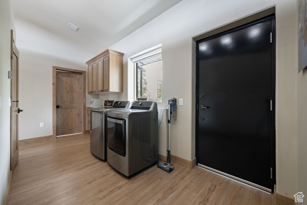 Washroom featuring washing machine and dryer, light wood-type flooring, cabinet space, and baseboards