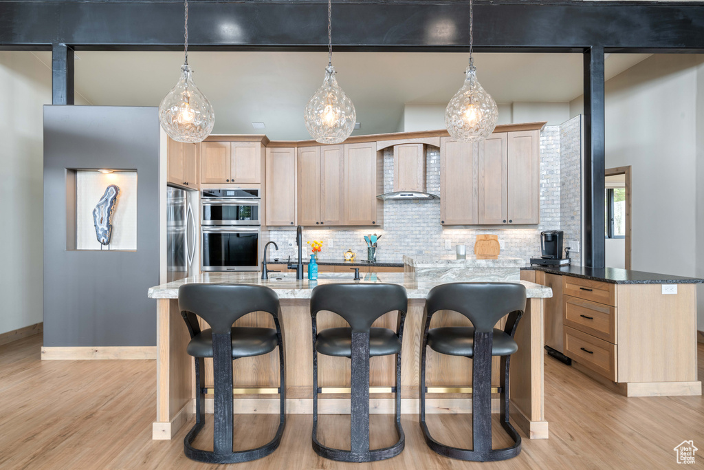 Kitchen with appliances with stainless steel finishes, light brown cabinets, light wood-style flooring, and backsplash