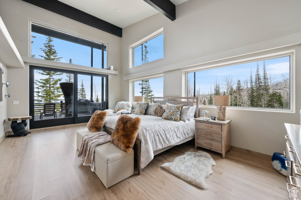Bedroom featuring access to exterior, beamed ceiling, light wood-style floors, and a high ceiling