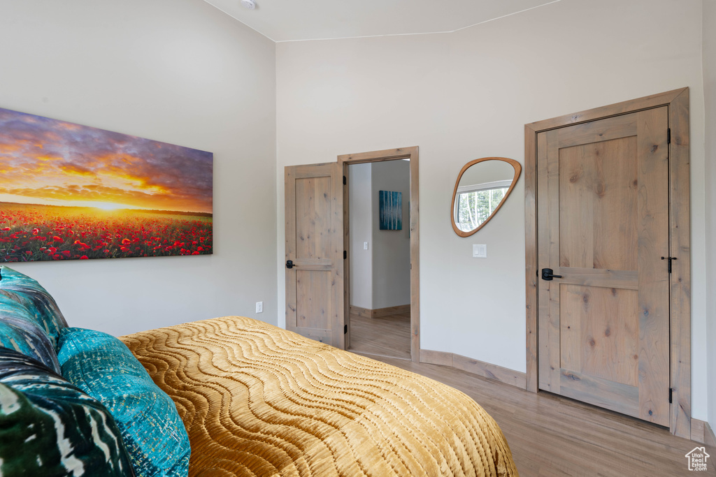 Bedroom with light wood finished floors, a towering ceiling, and baseboards