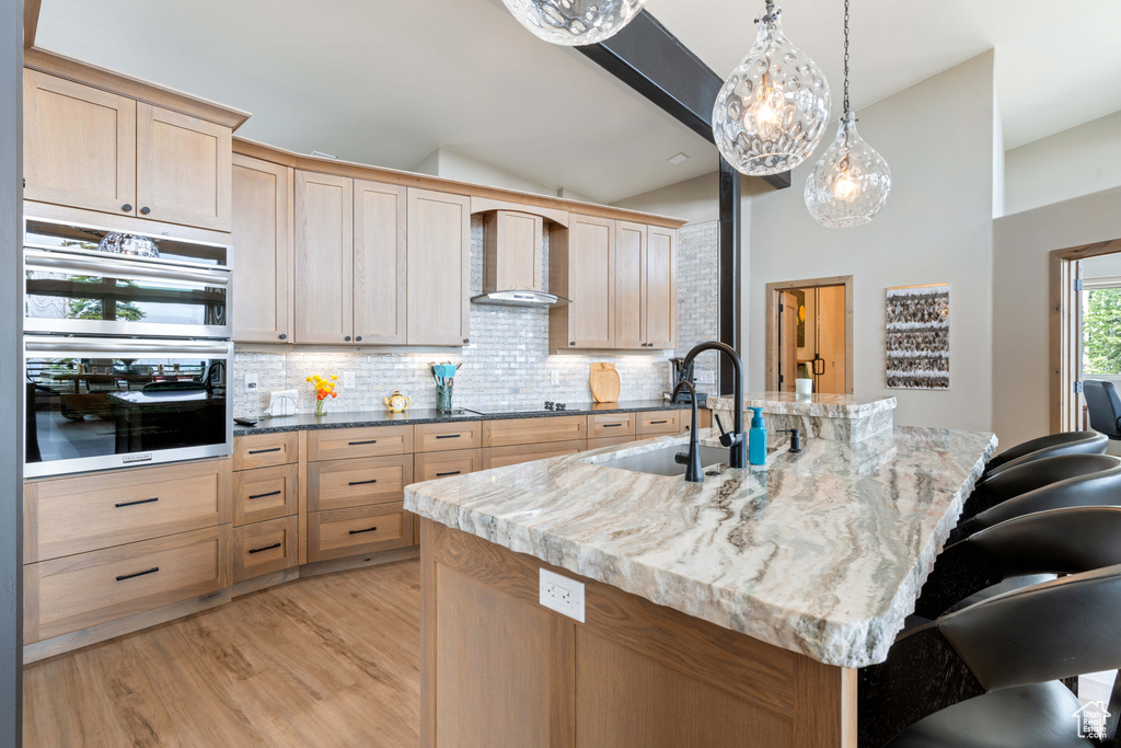 Kitchen featuring a sink, wall chimney exhaust hood, backsplash, light brown cabinetry, and lofted ceiling