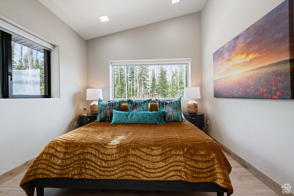 Bedroom with wood finished floors, lofted ceiling, multiple windows, and baseboards