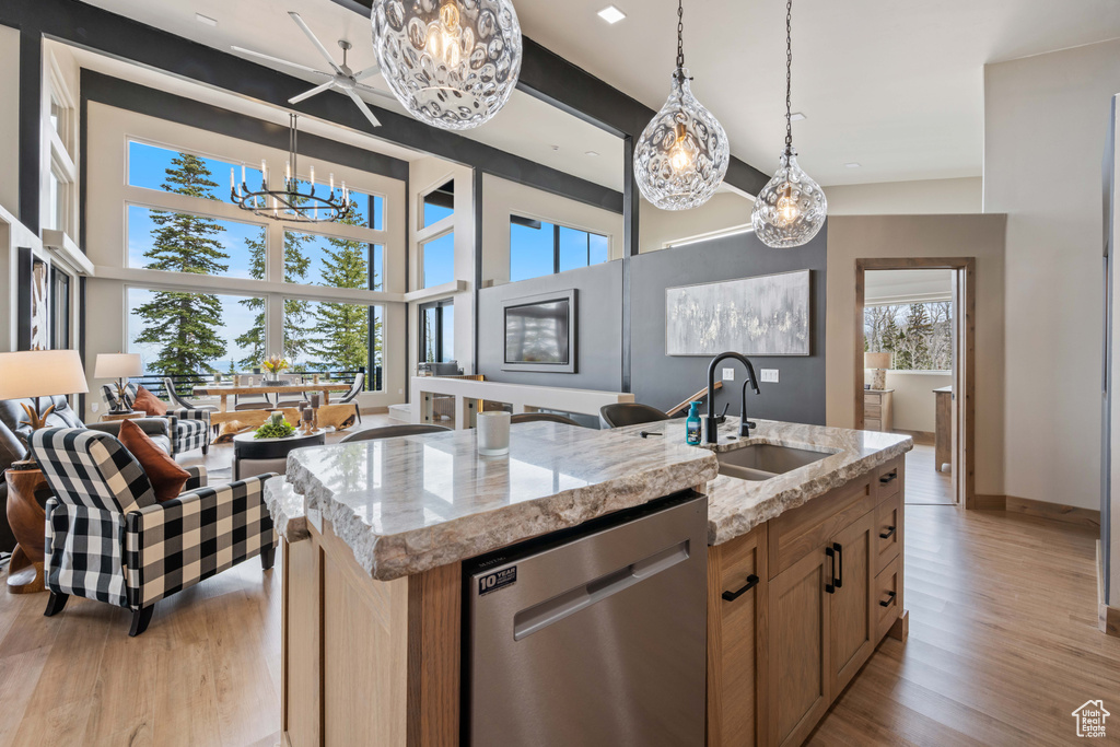 Kitchen with stainless steel dishwasher, a sink, a chandelier, light wood-style floors, and light stone counters