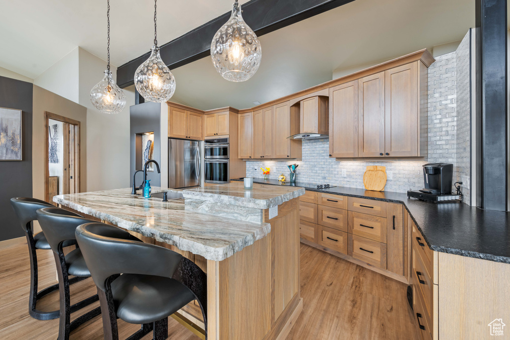 Kitchen featuring wall chimney exhaust hood, light brown cabinetry, stainless steel appliances, and light wood-type flooring