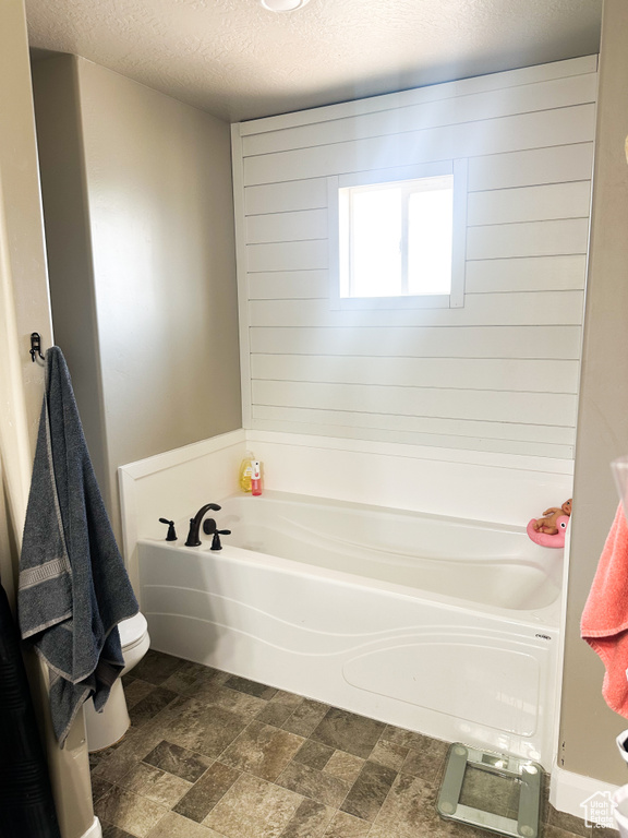 Full bath featuring a garden tub, a textured ceiling, and stone finish flooring