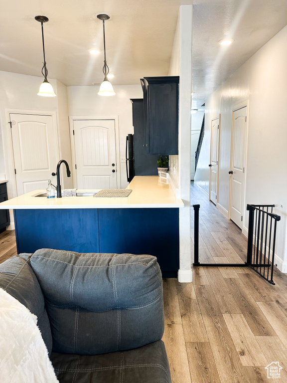 Kitchen with light wood-style floors, light countertops, freestanding refrigerator, a peninsula, and pendant lighting