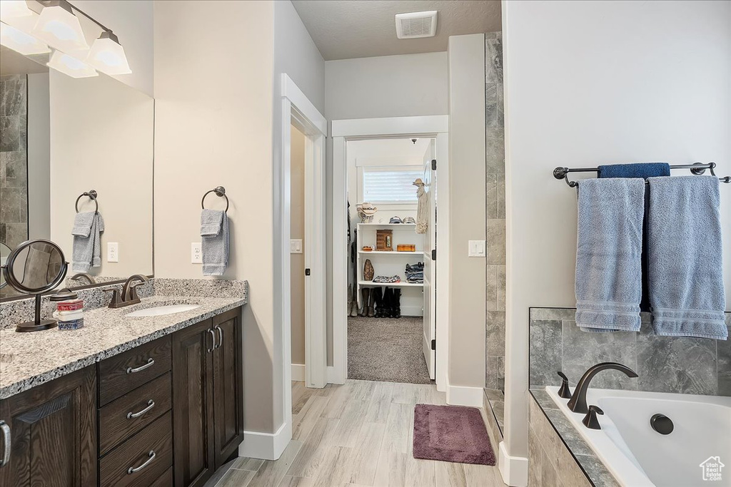 Bathroom featuring a bath, vanity, wood finished floors, baseboards, and tiled shower