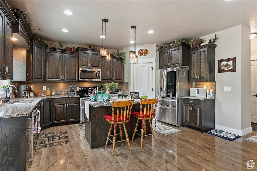 Kitchen with appliances with stainless steel finishes, a sink, dark brown cabinets, a center island, and tasteful backsplash