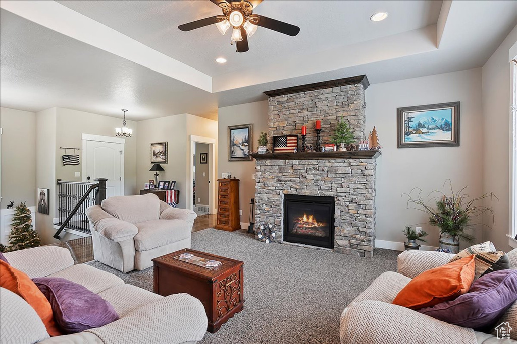 Carpeted living area featuring a raised ceiling, baseboards, ceiling fan, a fireplace, and a chandelier