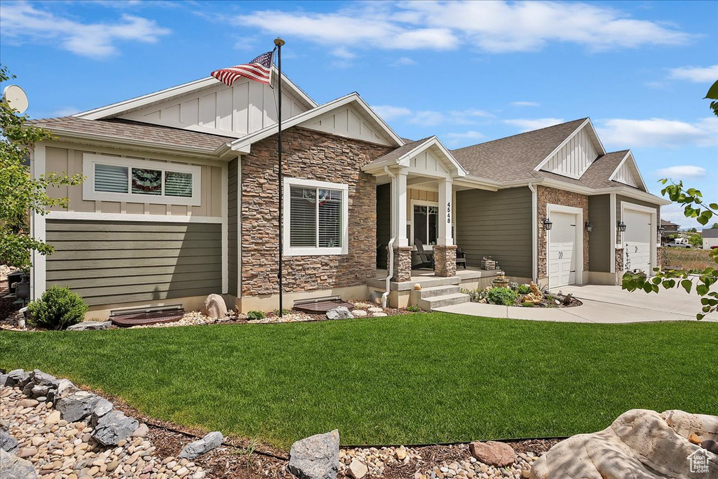 Craftsman house with board and batten siding, stone siding, driveway, and a front yard