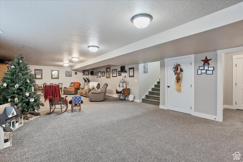 Living area with a textured ceiling, carpet flooring, stairs, and baseboards