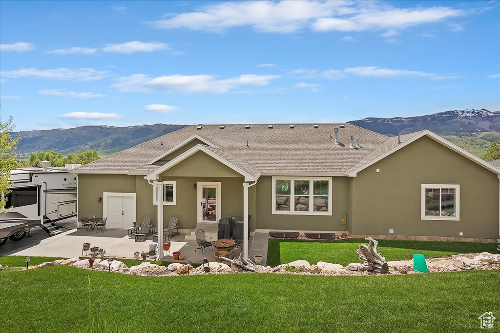 Back of house with a mountain view, stucco siding, a patio, and a lawn