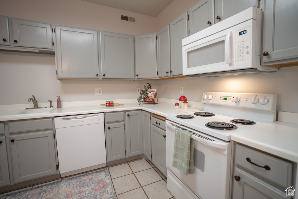 Kitchen with white appliances, a sink, gray cabinets, and light countertops