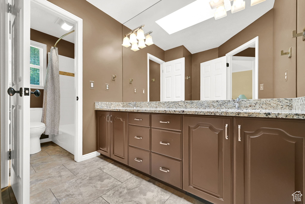 Full bathroom featuring toilet, double vanity, shower / tub combo, baseboards, and a skylight