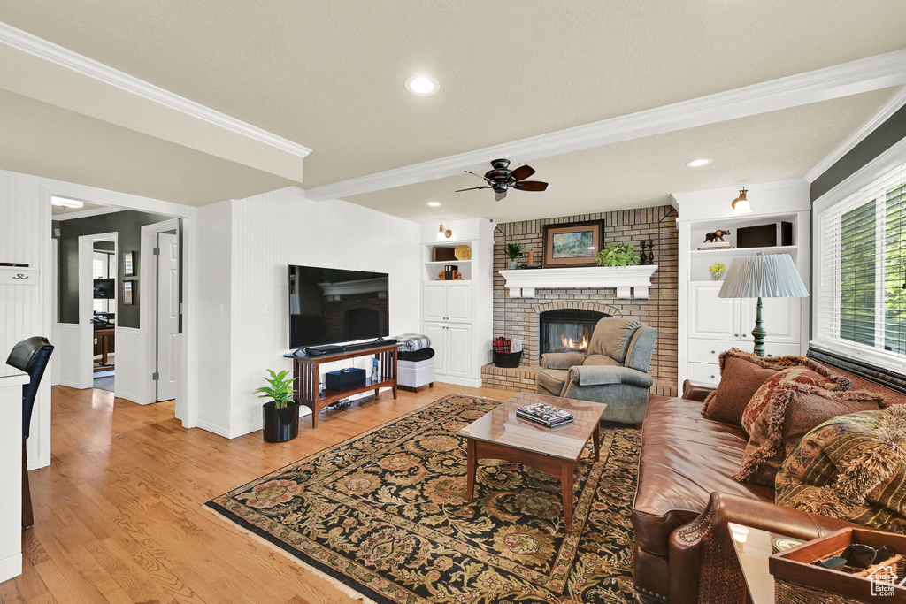 Living area with a brick fireplace, crown molding, a ceiling fan, baseboards, and light wood finished floors