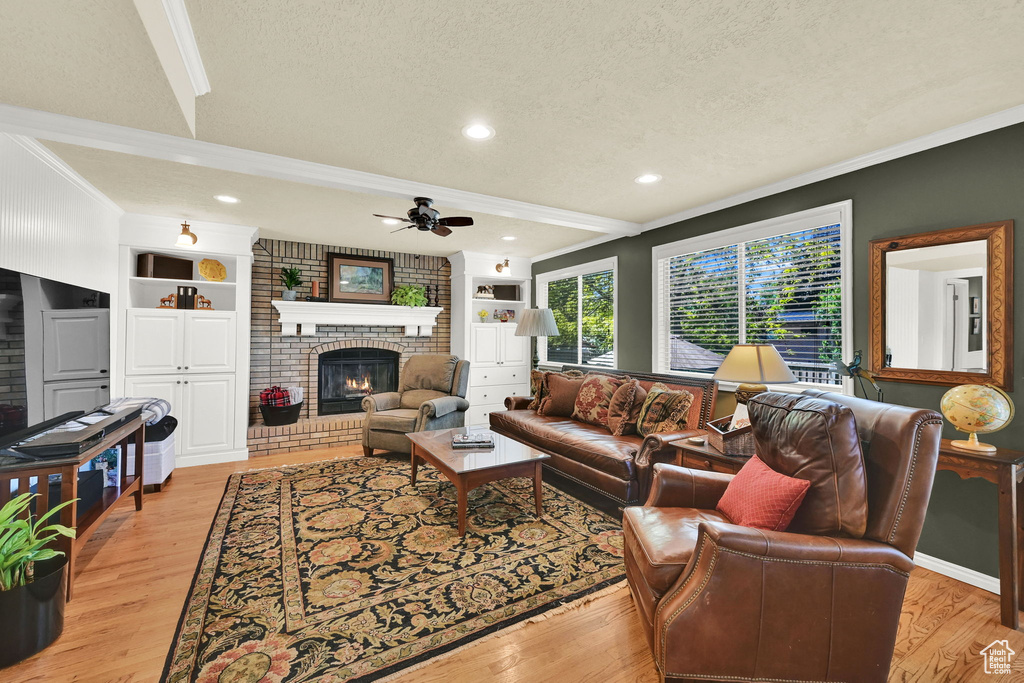 Living area featuring ornamental molding, a fireplace, a ceiling fan, light wood-type flooring, and a textured ceiling