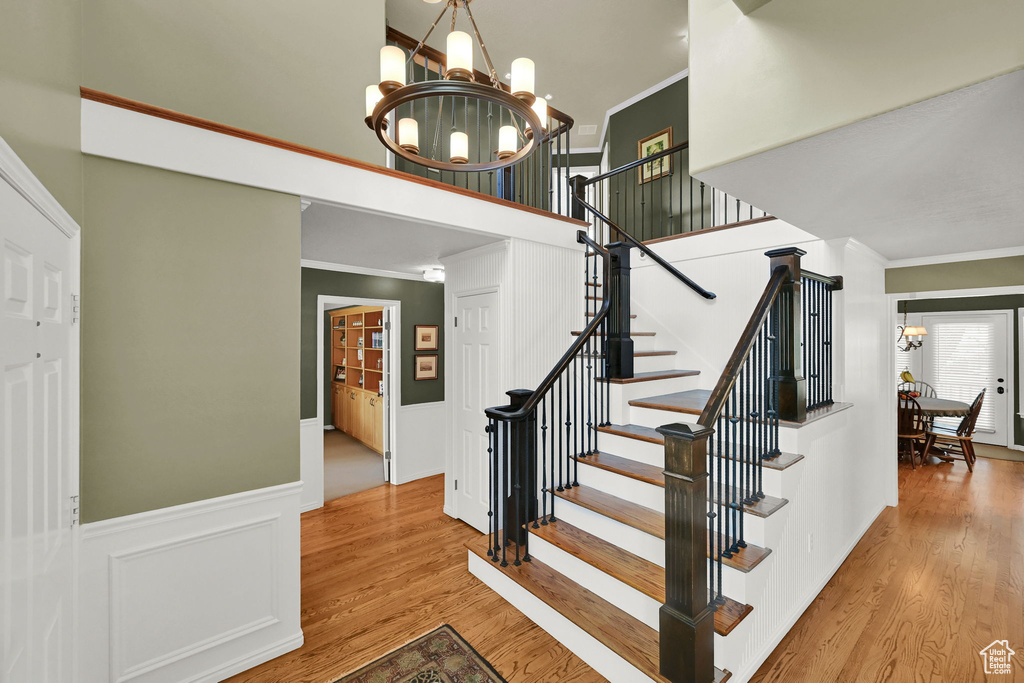 Stairway featuring a chandelier, ornamental molding, wood finished floors, a wainscoted wall, and a towering ceiling