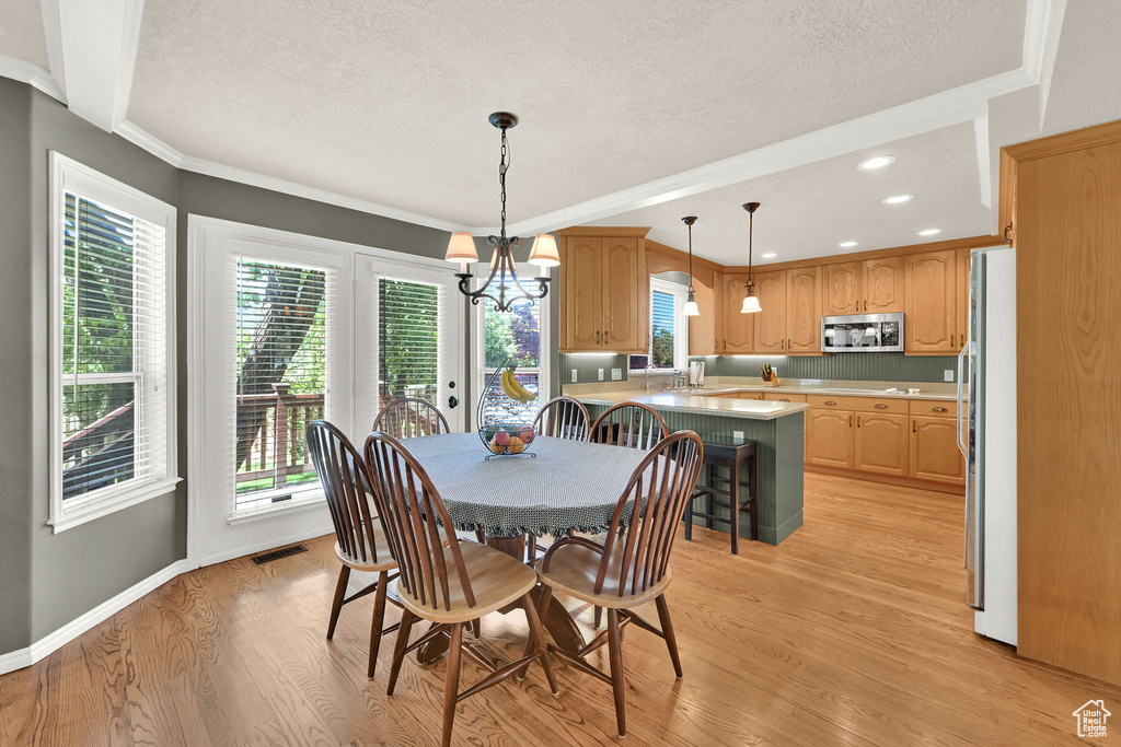 Dining room with a textured ceiling, light wood-style flooring, crown molding, a chandelier, and recessed lighting