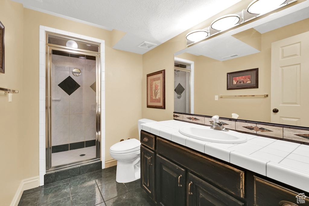 Bathroom featuring a shower stall, toilet, baseboards, and a textured ceiling