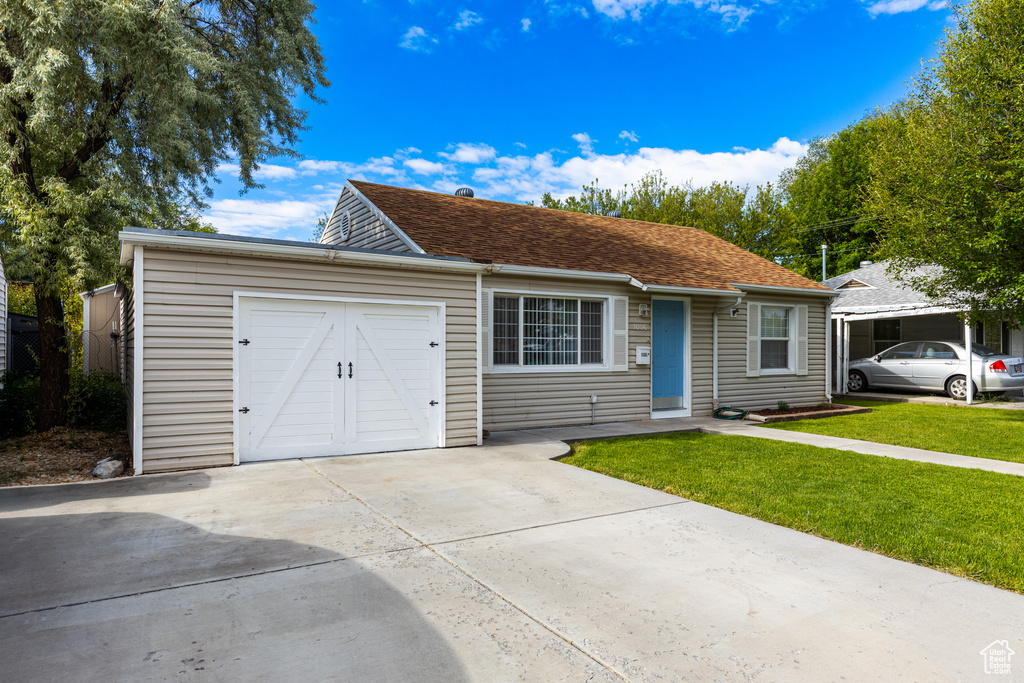 Ranch-style home featuring concrete driveway, a garage, and a front lawn